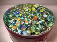 Photo showing a close-up of assorted glass marbles in a red metal tin.