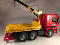 Side angle of red and yellow Bruder Mercedes tow truck showing crane arm extended and side decal details.