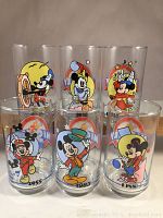 Front view of six vintage Sunoco Mickey Mouse commemorative glasses with colorful Mickey designs and year markings, displayed in two rows.