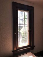Closed leaded glass window with wooden dark stain frame and brass handle hardware, fitted inside a textured wall.