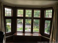 Front view of entire bay window assembly installed in alcove, showing all ten leaded glass panels and wood bench radiator cover below.