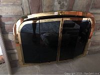 Full front view of the brass fireplace screen with three panels closed and brass frame visible.