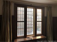 Three tall, rectangular leaded glass windows grouped together, each divided into grid panes with brass hardware and wooden frames. Visible windowsill and partial curtain sides.