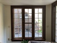 Three large wooden French pane style windows installed side by side inside a room, natural light visible, wall and floor partially visible