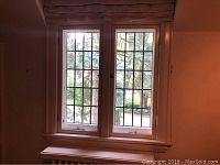Two tall original leaded glass windows with grid pattern leaded glass panels and cream painted frames with sills, installed in wall with soft pink color.