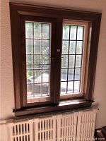 Two leaded glass windows with wooden frames and brass hardware installed in a wall. Lightly stained wood appears in good condition. One window has the interior hinged screen visible.