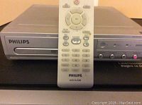 Front view of Philips DVD player with remote control placed upright on front.