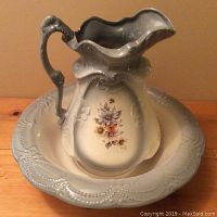 Photo showing light blue ceramic pitcher with ornate handle and floral motif, inside matching wash bowl with scalloped edge