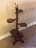 Vintage six-tier wooden plant or display stand with paddle-shaped tiers and a turned column base, standing against a beige wall on carpet.