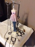 Photo of various silver necklaces hanging on mannequin jewelry display stand with pink top and blue jeans.