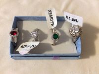 Four rings in a blue box, showing each with code tag and different jewel colors.