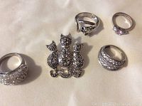 Set of four rings and a cat-shaped marcasite brooch arranged on light fabric