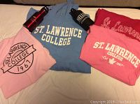 Photo of blue hoodie, two pink T-shirts, dark pink sweater, and two water bottles on couch