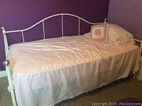 Front and side view of white metal Victorian style day bed with pink bedding and decorative pillow