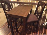 Photo showing full set of wood bar height table and two matching chairs on wood floor.