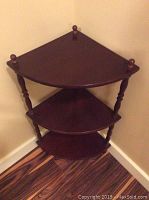 Full view of wood corner shelf from front left angle showing three triangular shelves and turned spindle supports.