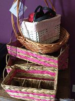 Photo showing six wicker baskets stacked including rectangular baskets with pink woven accents, white basket with fabric lining, and natural wicker trays.