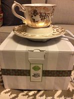 Scentsy electric warmer shaped like a teacup and saucer with gold floral design placed on its box.