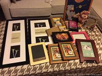 Photo showing a variety of picture frames in black, gold, wooden, pink, and green, arranged on a patterned surface