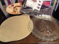Photo showing all items stacked on a table—pizza stone, silicone dessert pan in bag, Christmas tree glass platter, and veggie/chip tray with grape decoration.
