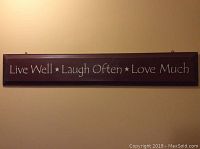 Full view of the rectangular wooden sign painted in dark brown with white text 'Live Well Laugh Often Love Much'.