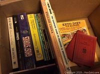 Books arranged in box titled on spine with various subjects including keto diet, ghost stories, collectibles, Shakespeare plays.