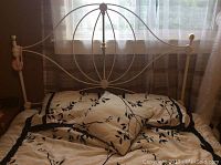Queen size bed dressed with black and white comforter, pillow shams, and decorative cushion. Comforter and shams show black leafy branch design on white background with black border.