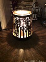 Lit Scentsy warmer showing forest tree cutout shadow effect illuminating warmly.