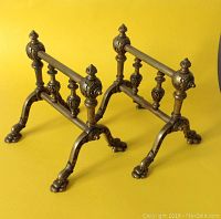 Pair of solid brass andirons shown against a yellow background, highlighting their Victorian ornate detailing and sturdy build.