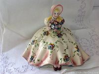Front view of the figurine showing the woman in a wide floral dress with bouquet and bonnet
