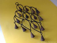 Full front view of antique hand-forged iron wind chimes set against yellow background showing diamond lattice frame and attached conical bells.