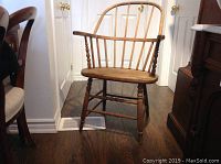 Front view of the antique wooden Windsor chair showing slightly curved arms, spindle back, and turned legs.