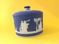 Side view of antique Wedgwood jasperware lidded jar showing classical white relief figures and trees on matte blue ground