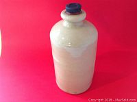 Front view of off-white English Victorian stoneware bottle with narrow neck and black stopper