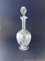 Full view of the clear cut crystal decanter with stopper against a dark background.