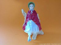 Front view of Royal Doulton 'Sally' figurine showing the seated woman in bonnet and cape.