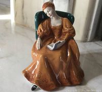Front view of the Royal Doulton 'Romance' figurine showing seated woman in orange dress reading a book.