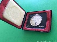 Open display case showing the silver dollar coin in black holder with red inner lining and foam padding on lid.