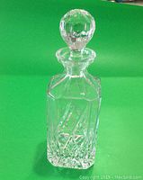 Full view of clear cut crystal decanter with faceted stopper on green background.