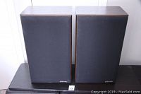 Pair of Polk Monitor 7 speakers with fabric grilles on, showing wood grain sides and front branding.