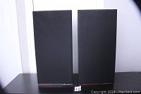 Front view of both speakers with grilles installed, showing black cloth covers and walnut veneer bases.