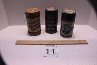 Three Edison cylinder records in their original cylindrical cardboard containers, placed behind a ruler for scale.