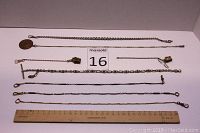 Top view of 8 assorted pocket watch chains and fobs laid flat with measuring ruler.