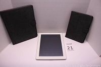 Front view of white Apple iPad 2 between two black folio cases of different sizes. Larger case to left matches iPad 2 size, smaller case right matches iPad Mini size.
