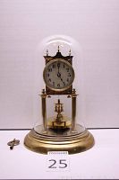Full front view of clock under glass dome on stepped brass base with winding key beside it