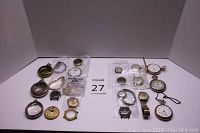 Full lot display with assortment of watch parts, wristwatches, pocket watches, and cases arranged against white background