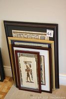 Lot of 4 framed Egyptian-themed papyrus artworks stacked on floor showing varied frame styles and sizes