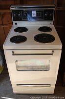 Front view of off-white General Electric electric stove showing four coil burners and oven door with window.