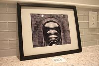Framed black and white photograph showing architectural stone arches in perspective, placed on kitchen countertop.