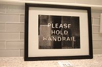 Framed black and white photo showing the text 'PLEASE HOLD HANDRAIL'.